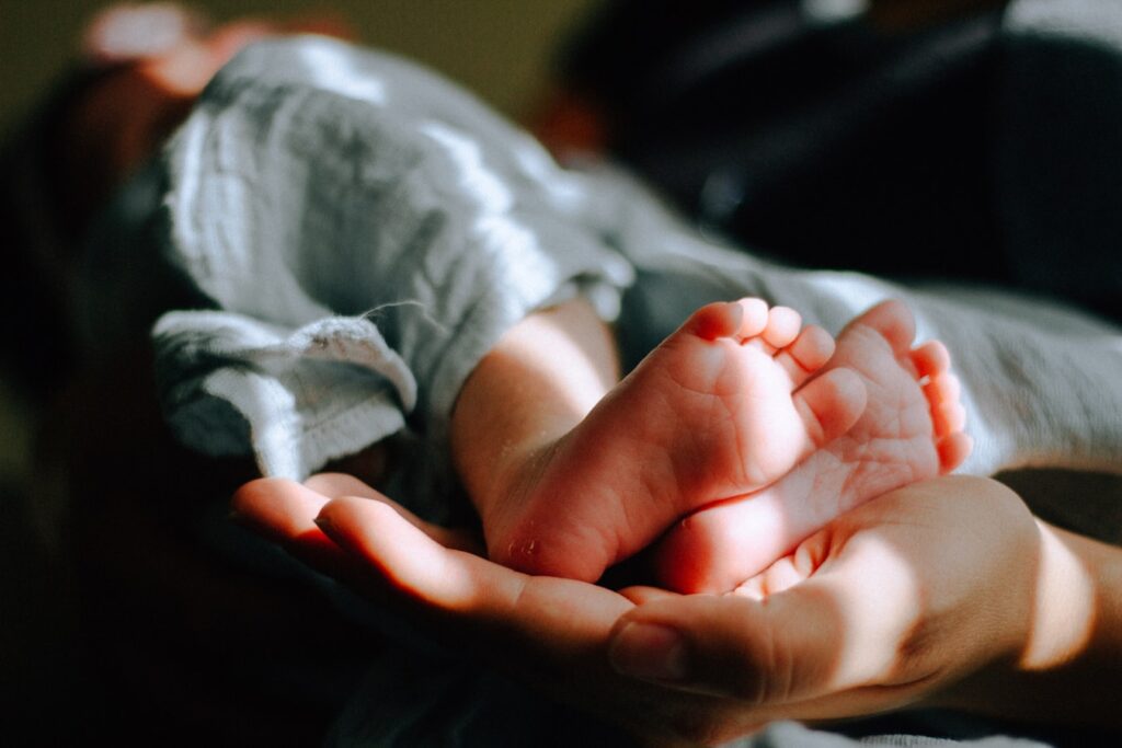 mama trzyma na swojej dłoni małe stópki niemowlęcia