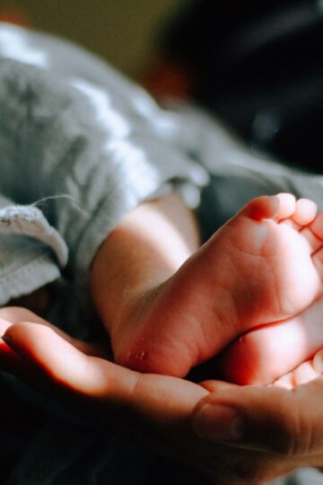 mama trzyma na swojej dłoni małe stópki niemowlęcia